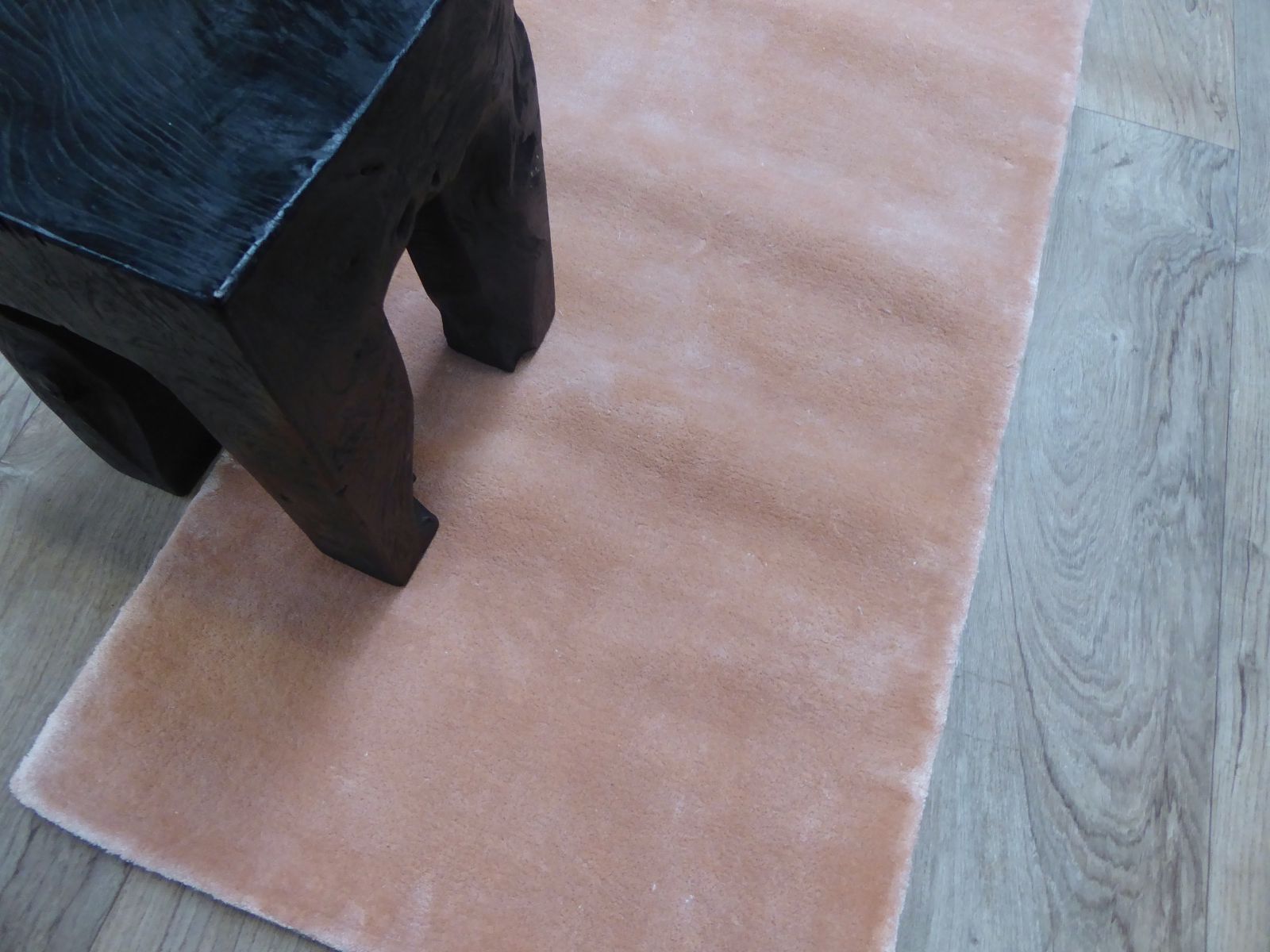 Tapis en viscose pêche rose avec un tabouret noir, apportant chaleur et élégance à la décoration intérieure