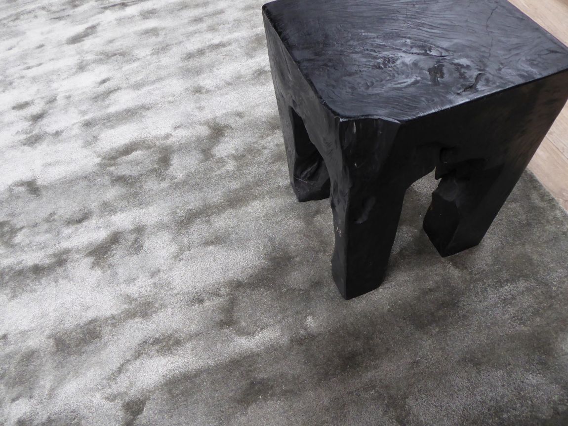 Tapis gris en viscose accompagné d'un tabouret en bois noir, apportant élégance et chaleur 