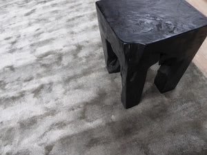 Tapis gris en viscose accompagné d'un tabouret en bois noir, apportant élégance et chaleur 