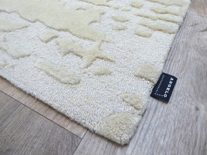 Tapis ivoire texturé en laine et viscose, à motifs abstraits en relief, photographié en angle pour montrer l’épaisseur et les reflets