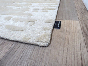 Tapis ivoire à motifs abstraits en relief, vue d’angle mettant en valeur l’épaisseur et le contraste des textures