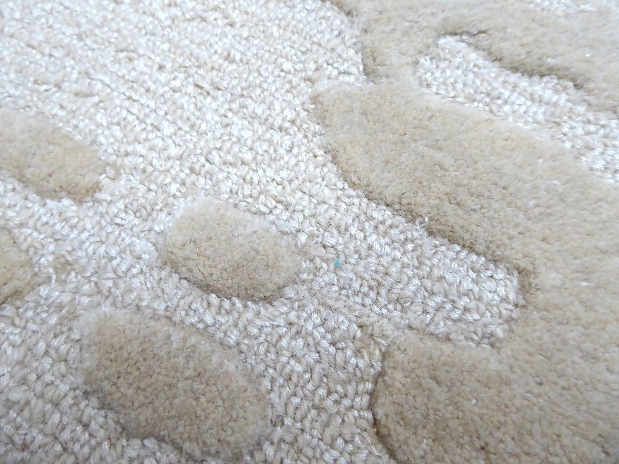 Détail du tapis ivoire en laine et viscose, gros plan sur les nuances de texture et de brillance et les motifs abstraits doux en relief