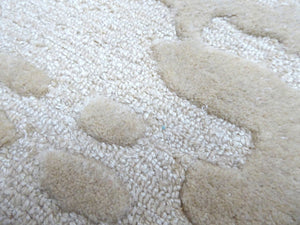 Détail du tapis ivoire en laine et viscose, gros plan sur les nuances de texture et de brillance et les motifs abstraits doux en relief
