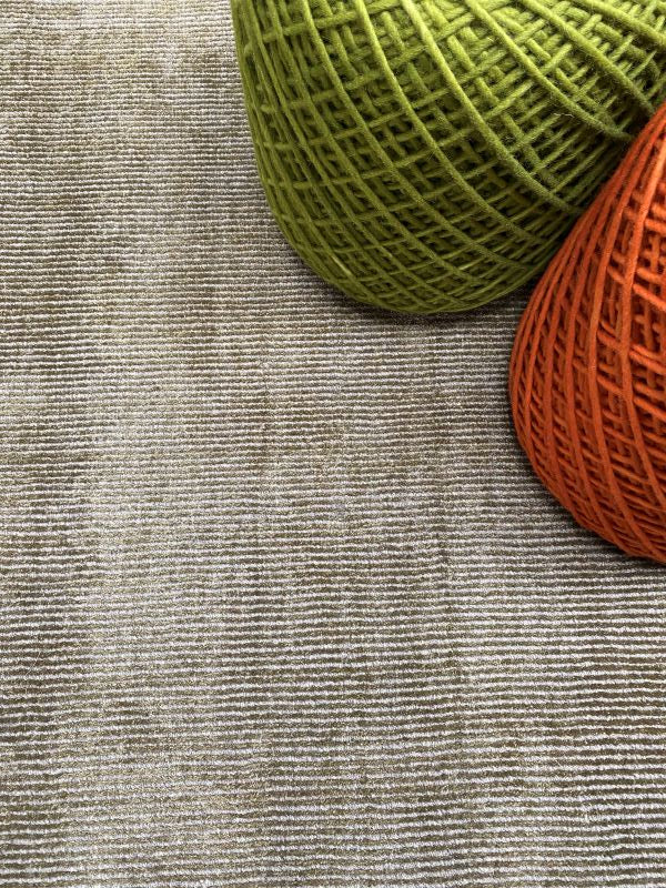 Tapis argent vert brillant intégré dans un salon avec des poufs, créant une ambiance chaleureuse et sophistiquée