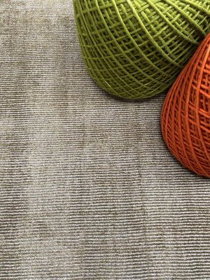 Tapis argent vert brillant intégré dans un salon avec des poufs, créant une ambiance chaleureuse et sophistiquée