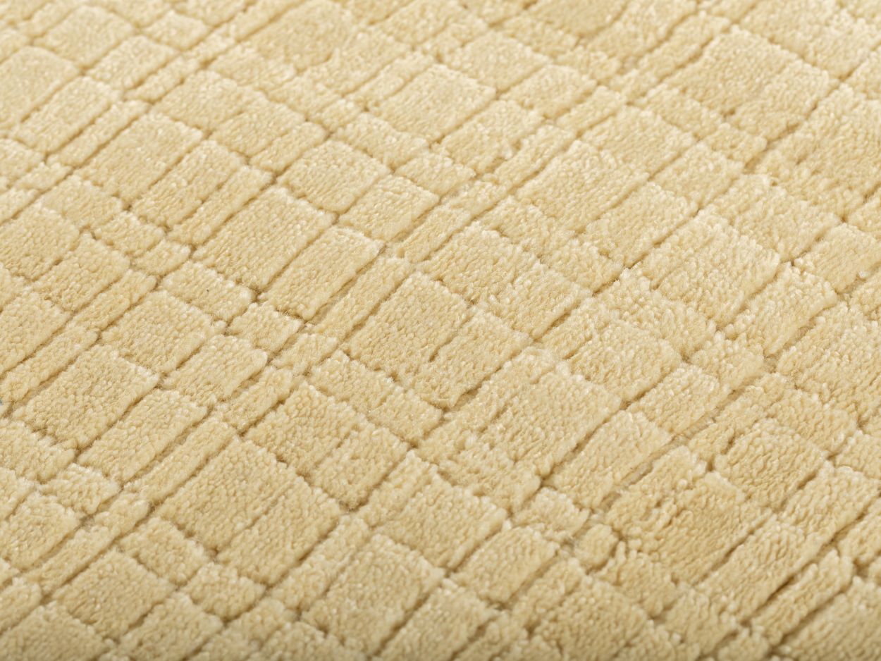 Gros plan du tapis beige jaune pâle montrant la texture tissée à la main en PET recyclé et son motif carreaux subtil