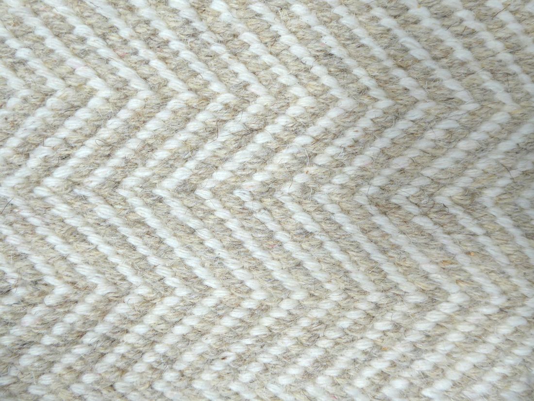 Détail du tissage artisanal du tapis en laine de Nouvelle-Zélande, motif zigzag géométrique subtil beige clair et blanc