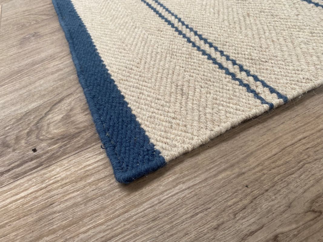 Détail d’angle du tapis tissé main beige rayé marine montrant la texture et la finition des bords