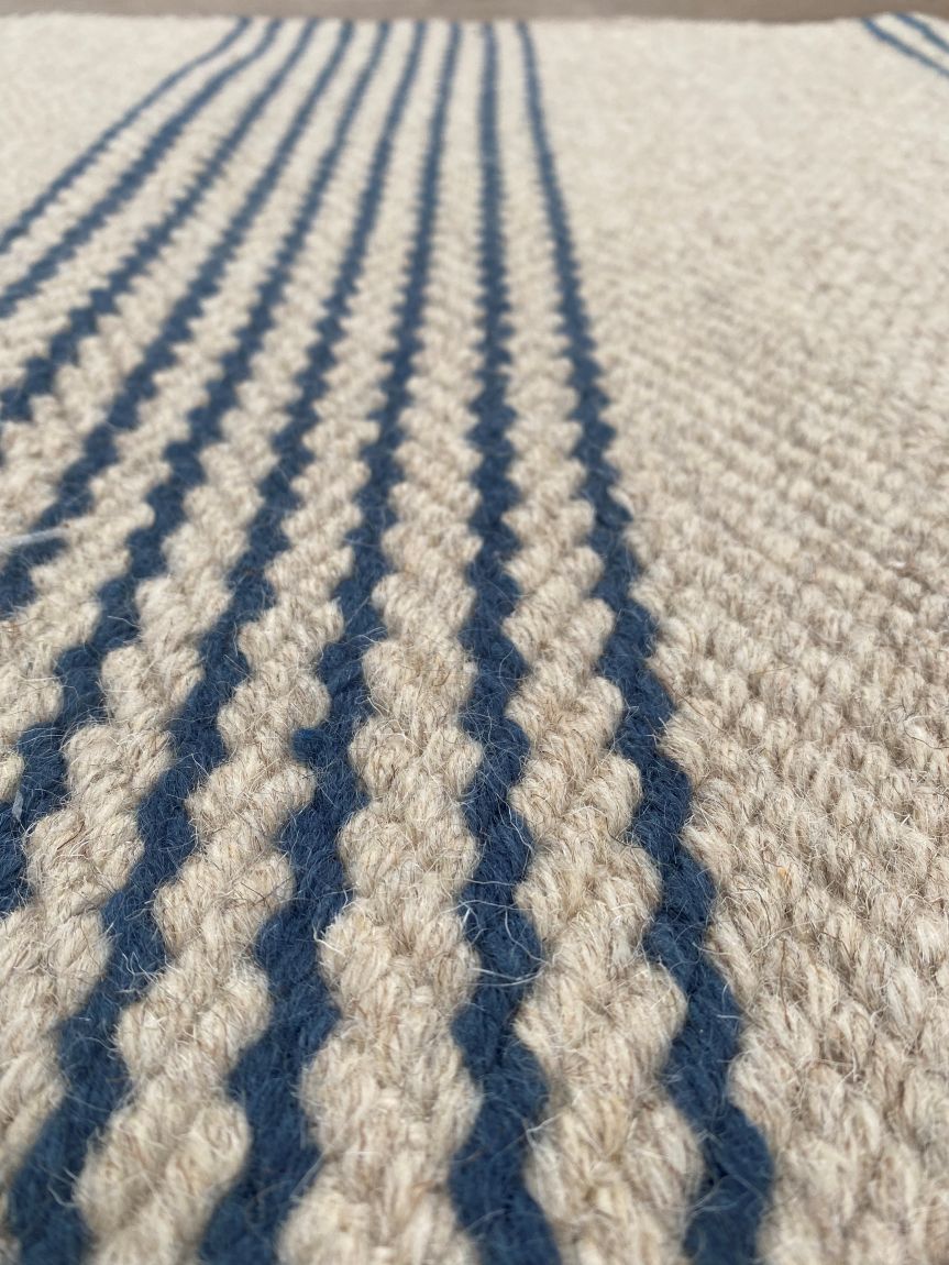 Gros plan sur le tissu du tapis tissé main beige rayé marine mettant en valeur la texture et les fibres