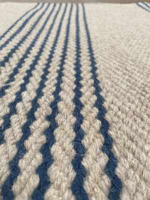 Gros plan sur le tissu du tapis tissé main beige rayé marine mettant en valeur la texture et les fibres