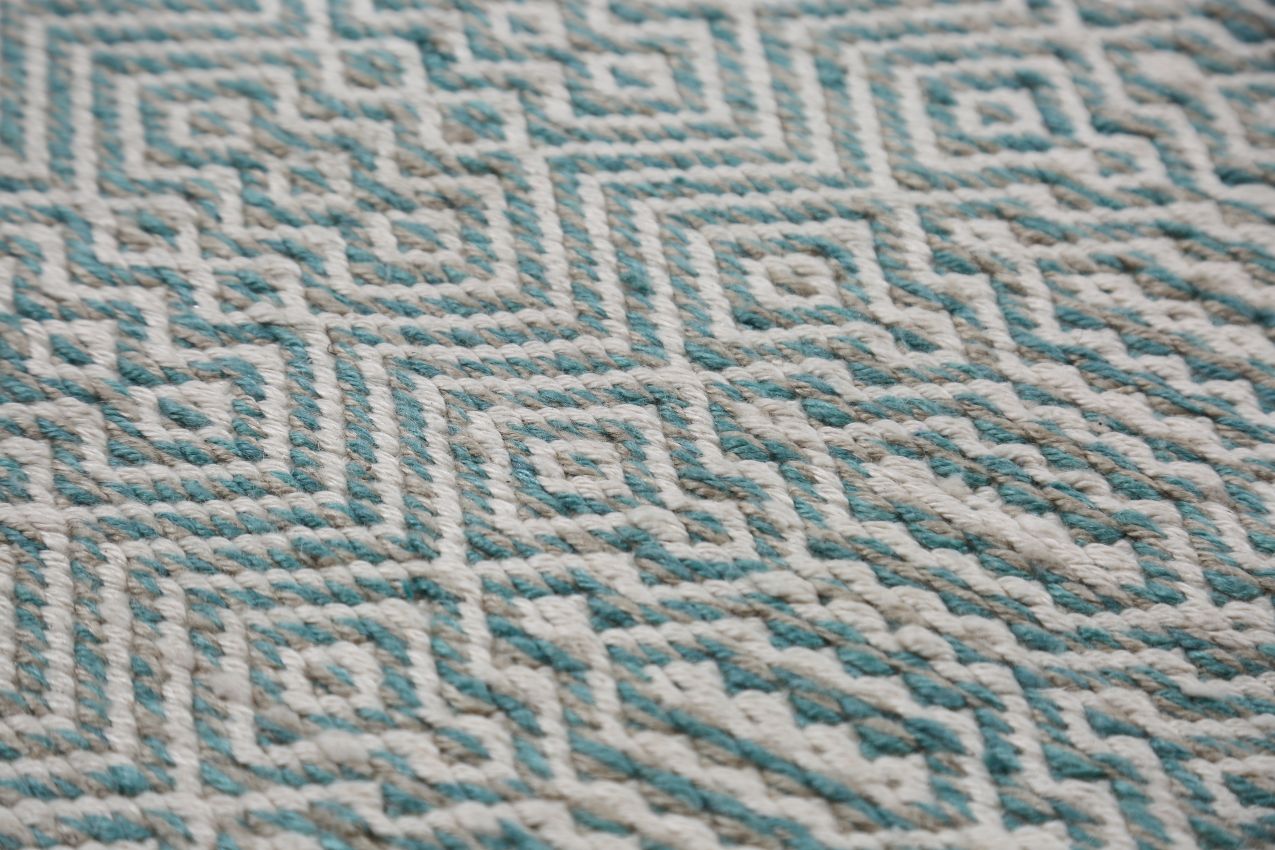 Gros plan sur motifs géométriques blanc et turquoise d’un tapis en PET recyclé, texture résistante, usage tout terrain