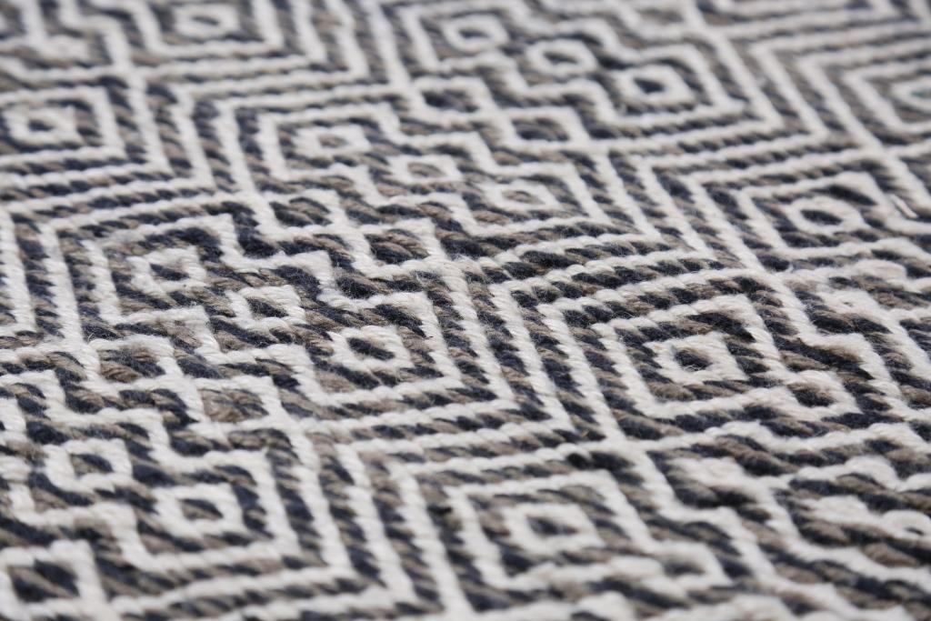 Gros plan sur les motifs géométriques du tapis en PET recyclé blanc, gris et marine, texture tissée résistante à extérieur