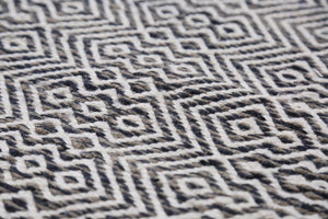 Gros plan sur les motifs géométriques du tapis en PET recyclé blanc, gris et marine, texture tissée résistante à extérieur