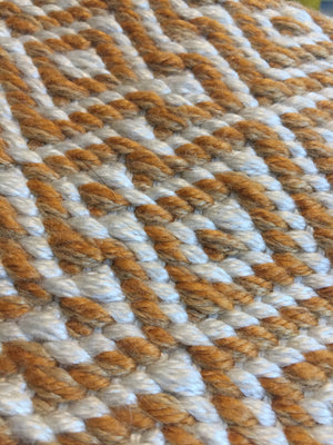 Het vloerkleed heeft een herhalend, etnisch en Scandinavisch geïnspireerd geometrisch ruitpatroon in oranje en crèmekleuren, duidelijk afgetekend tegen een egale witte achtergrond.

