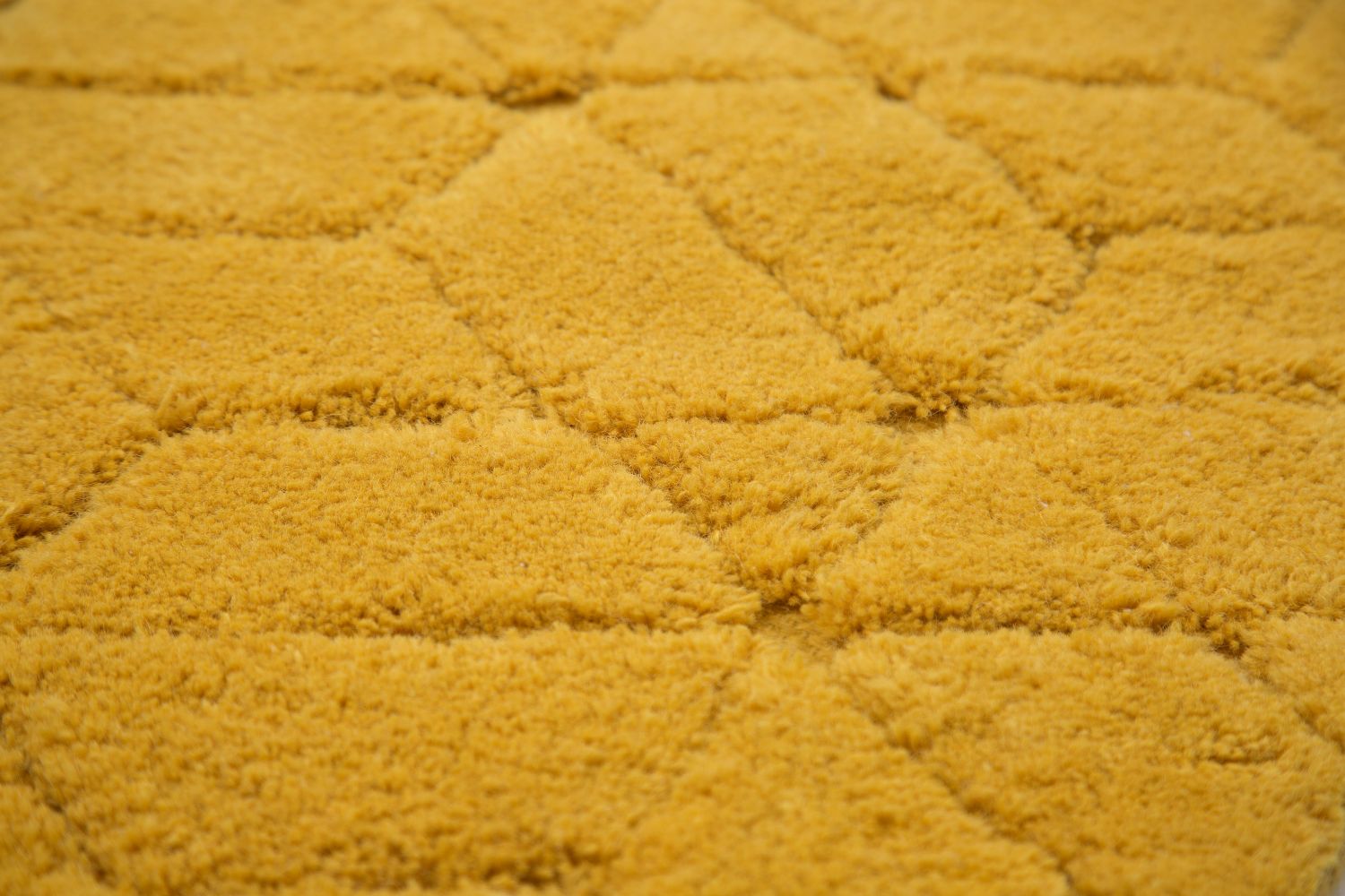Gros plan sur la texture du tapis en laine jaune, montrant les reliefs et les motifs géométriques tissés à la main