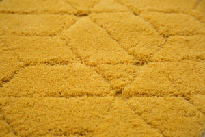 Gros plan sur la texture du tapis en laine jaune, montrant les reliefs et les motifs géométriques tissés à la main
