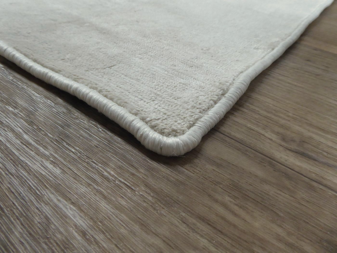 Tapis ivoire en soie de bambou vu en angle, montrant l’épaisseur, la bordure et la finition haut de gamme