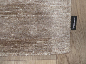 Gros plan sur la texture soyeuse du tapis en soie de bambou marron clair, révélant les fibres fines et la finition luxueuse