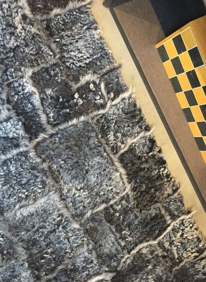 Tapis gris foncé en laine d’agneau, poil long et court, vu de bord