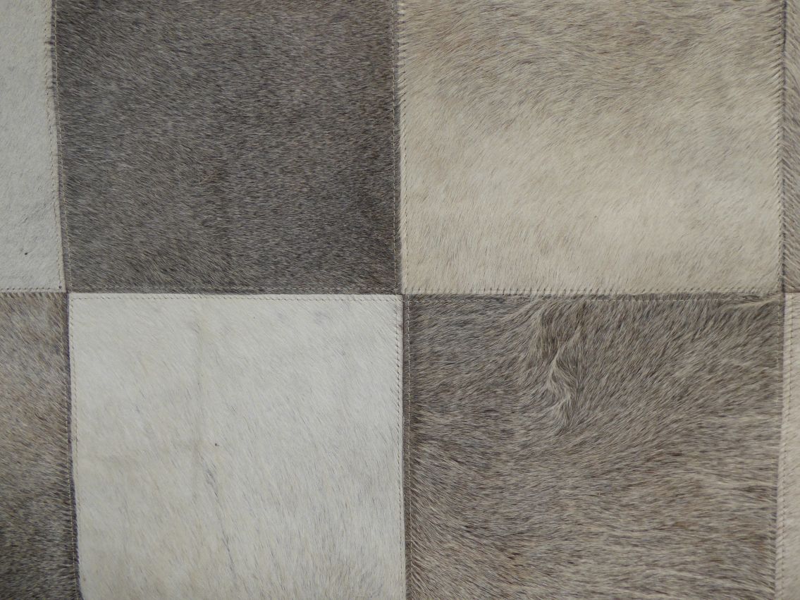Gros plan sur la matière du tapis en cuir de vachette montrant les nuances gris ivoire brun et la structure géométrique