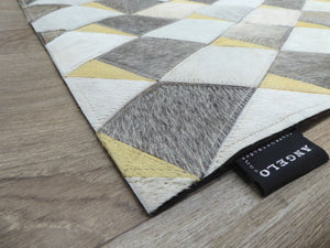 Détail d'angle du tapis en cuir de vachette avec motifs géométriques gris ivoire jaune