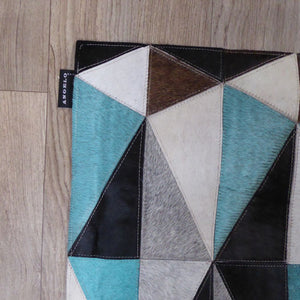 Tapis en cuir de vachette avec motifs géométriques gris, ivoire, bleu et brun – vue en angle montrant texture et bords