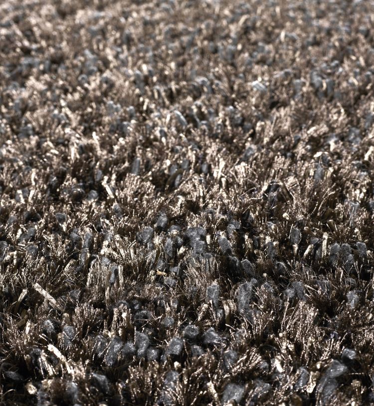 Gros plan sur le tapis à poils longs gris bronze, mettant en valeur la texture soyeuse et les reflets métalliques