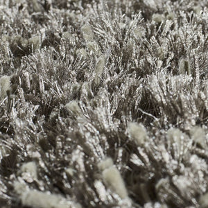 Détail rapproché du tapis gris brillant à poils longs, mettant en valeur la texture soyeuse et la lumière sur les fibres