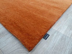 Tapis en laine orange tissé main, vu en angle pour révéler l’épaisseur et les détails du tissage artisanal