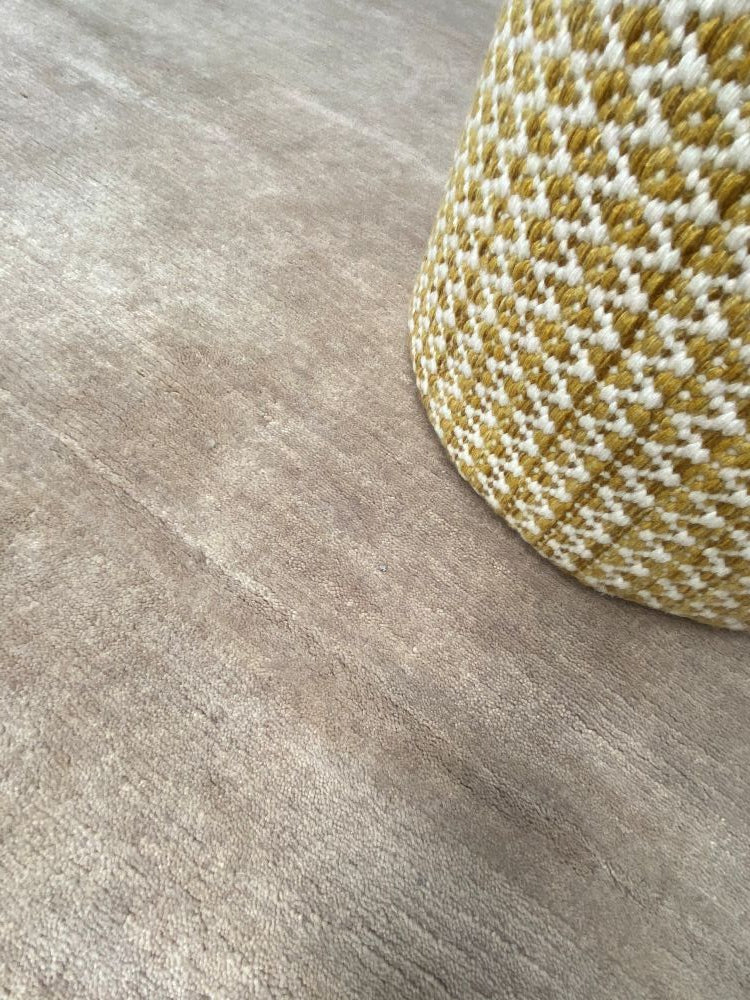 Tapis soyeux couleur sable en laine naturelle, présenté avec un pouf en décoration intérieure chaleureuse