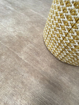 Tapis soyeux couleur sable en laine naturelle, présenté avec un pouf en décoration intérieure chaleureuse