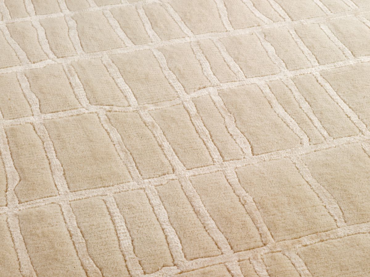 Gros plan sur la texture douce et la brillance du tapis beige en laine et viscose, révélant les motifs irréguliers