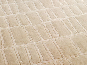 Gros plan sur la texture douce et la brillance du tapis beige en laine et viscose, révélant les motifs irréguliers