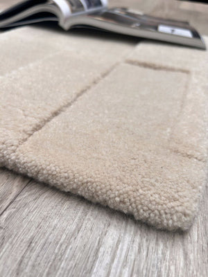 Détail du tapis en laine blanc cassé, texture douce et motifs géométriques en relief – gros plan sur le coin