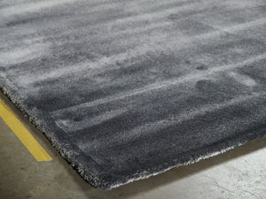 Vue en coin d’un tapis gris artisanal en viscose, mettant en valeur sa brillance et son tombé raffiné