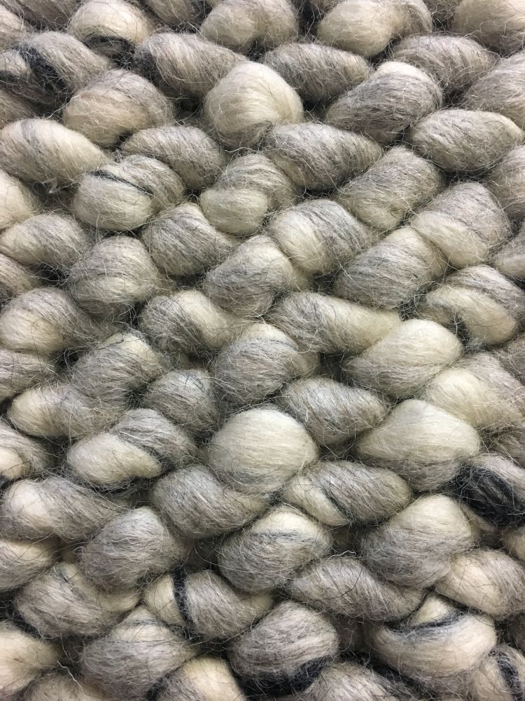 Gros plan sur les boucles en laine feutrée du tapis ivoire et gris, montrant le relief unique et la texture douce
