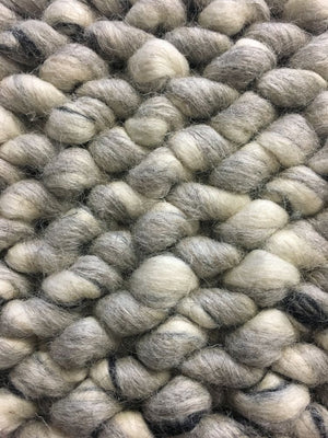 Gros plan sur les boucles en laine feutrée du tapis ivoire et gris, montrant le relief unique et la texture douce