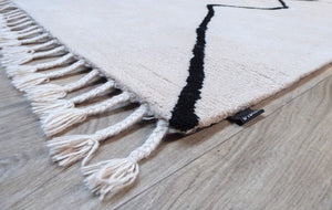 Détail d’un coin du tapis ivoire en laine avec franges et motif noir discret