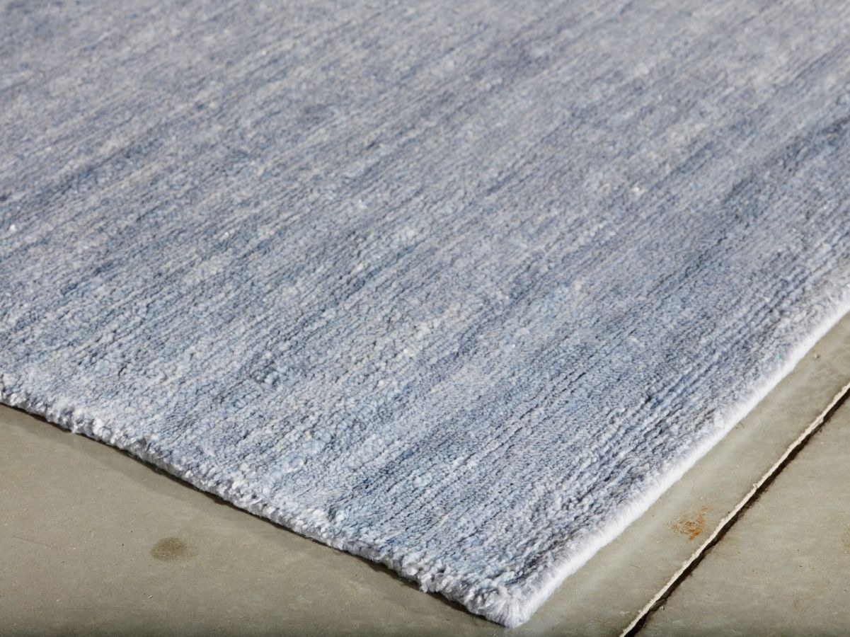 Vue en angle d’un tapis en soie de bambou bleu et blanc, montrant la texture brillante et les bords finis