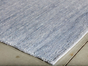 Vue en angle d’un tapis en soie de bambou bleu et blanc, montrant la texture brillante et les bords finis