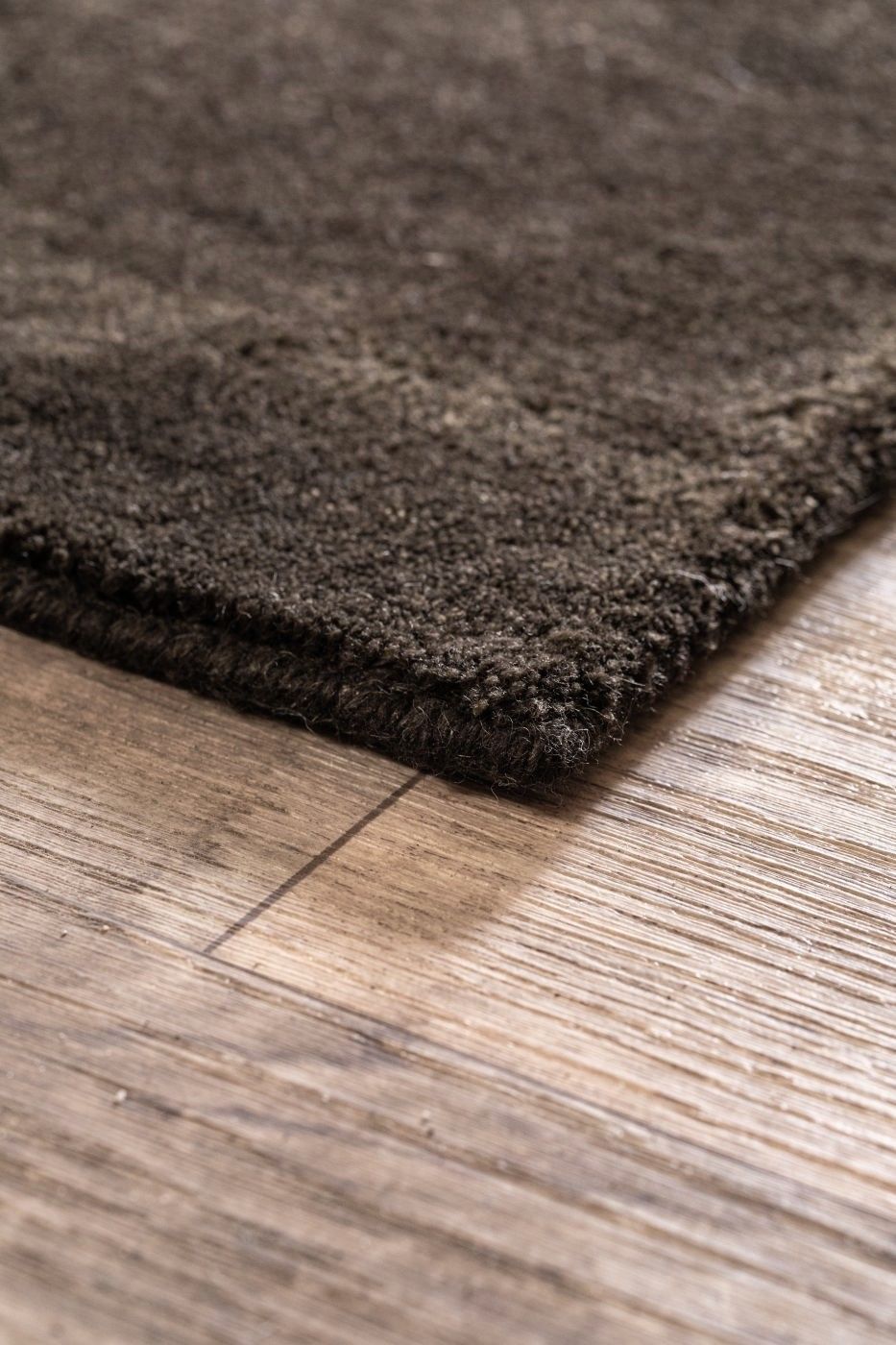 Vue en coin du tapis brun gris foncé tissé main en laine, montrant les bords et la finesse du tissage artisanal