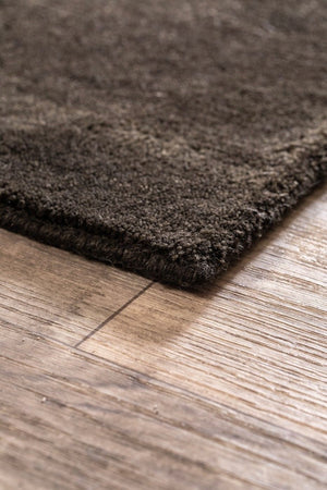 Vue en coin du tapis brun gris foncé tissé main en laine, montrant les bords et la finesse du tissage artisanal