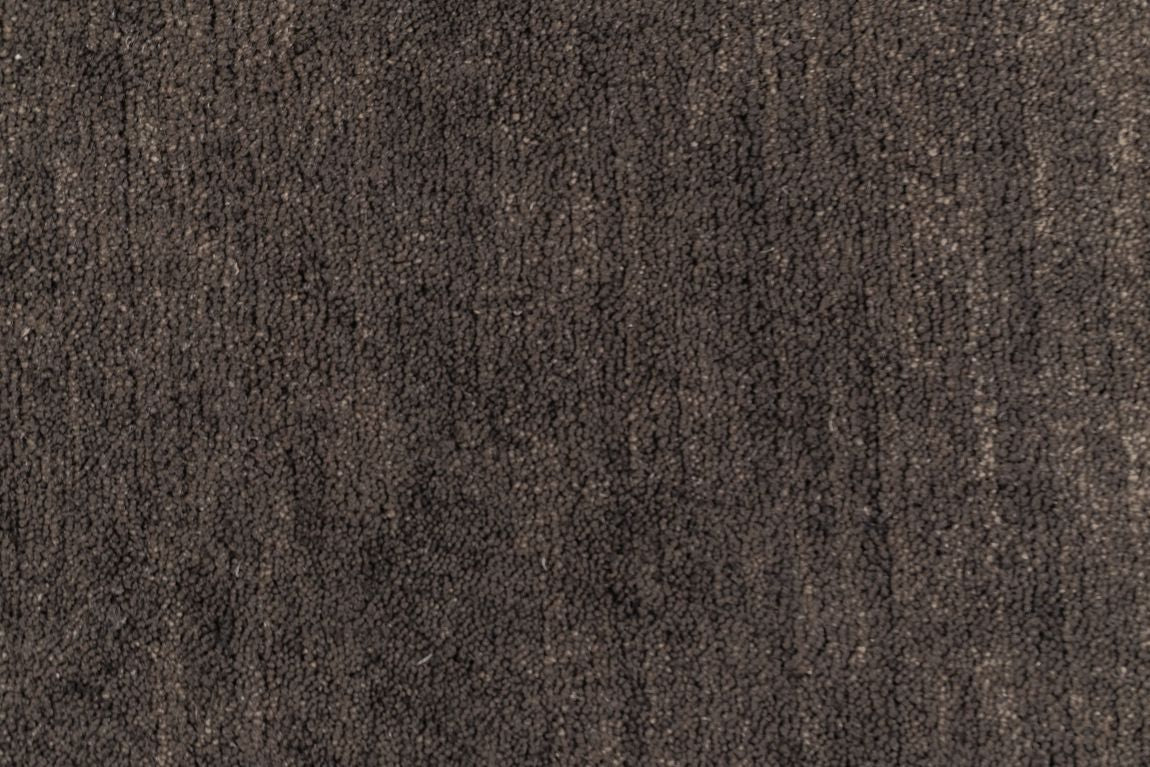 Gros plan sur la texture du tapis brun gris foncé tissé main en laine, révélant les fibres soyeuses et le travail artisanal détaillé