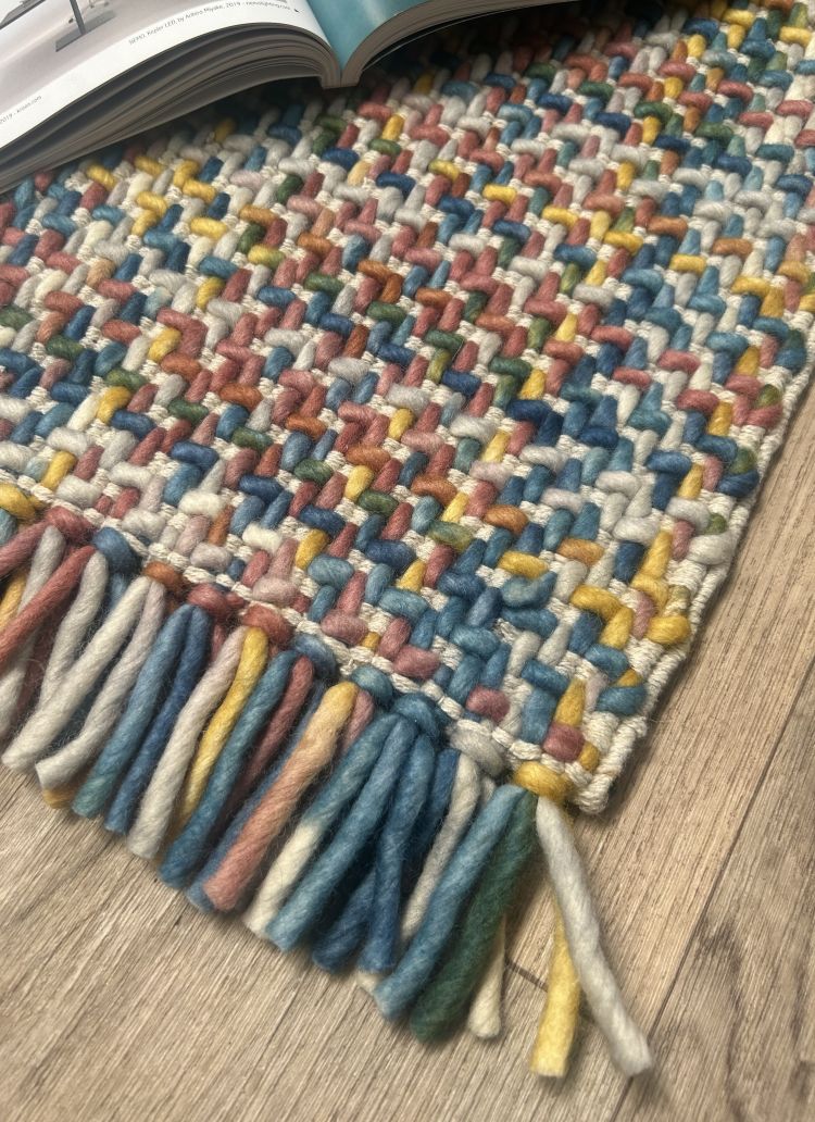 Tapis pastel en laine avec effet tweed-tartan et franges, présenté en vue de coin pour montrer épaisseur et texture