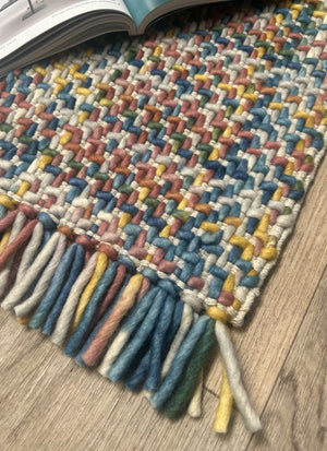 Tapis pastel en laine avec effet tweed-tartan et franges, présenté en vue de coin pour montrer épaisseur et texture