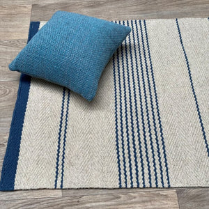 Tapis tissé main rayé beige et marine avec un coussin pour montrer son rendu décoratif