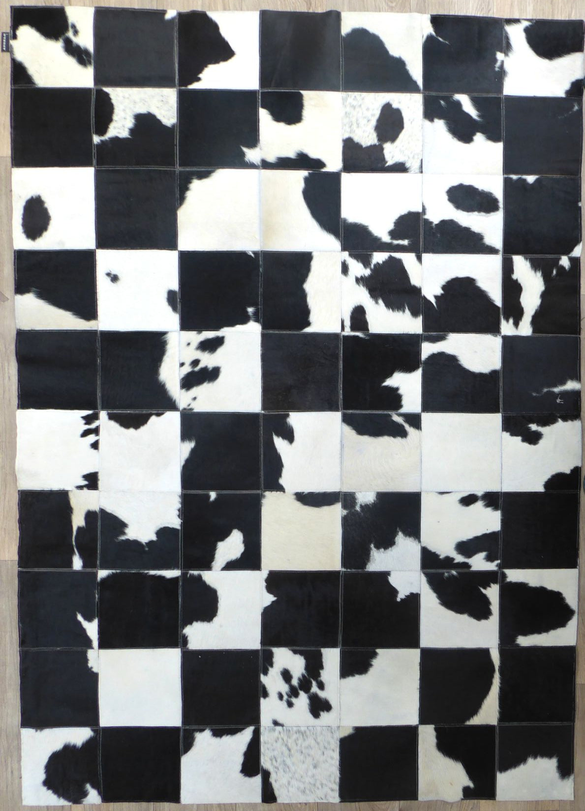 Tapis audacieux en cuir de vachette, motifs géométriques damier peau de vache gris ivoire noir, vue de face